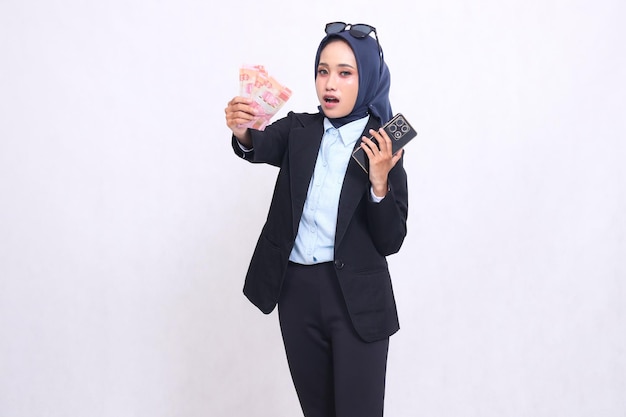 Inteligentna azjatycka kobieta z biura w hidżabie stoi w zaskoczeniu niosąc banknoty rupii i telefon komórkowy