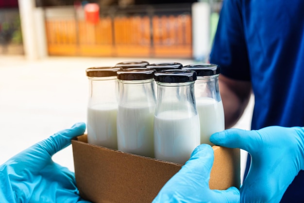 Zdjęcie inteligentna dostawa mężczyzna usług gastronomicznych podający pudełko mleka odbiorcy z kobietą klientką odbierającą zamówienie od kuriera w domu usługa wokera mleko zakupy online