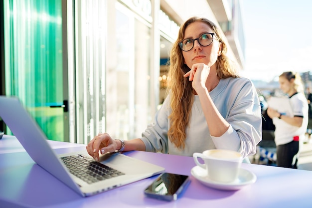 Inteligentna kobieta w okularach siedzi w kawiarni za pomocą laptopa