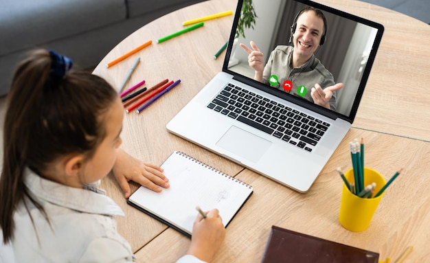 Inteligentna mała przedszkolanka ogląda lekcję online i komunikuje się z nauczycielem w domu, małe dziecko uczy się w Internecie za pomocą połączenia bezprzewodowego laptopa.