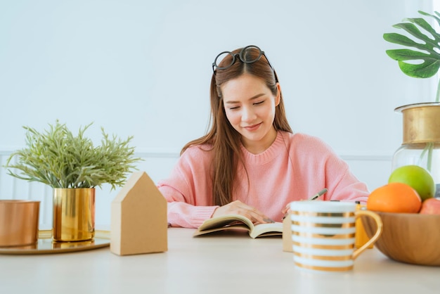 Inteligentna piękna dorywcza azjatycka kobieta cieszy się czytaniem książki weekend w różowym swetrze w tle domu