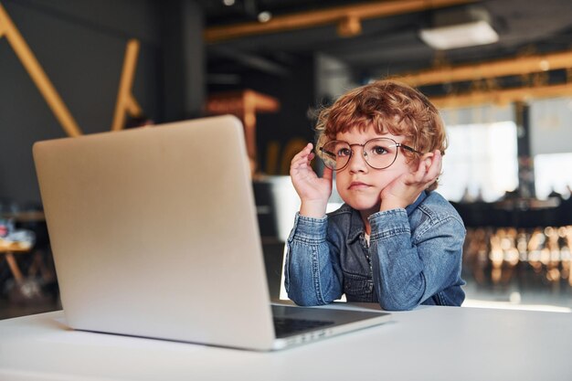 Inteligentne dziecko w zwykłych ubraniach i okularach korzystające z laptopa w celach edukacyjnych