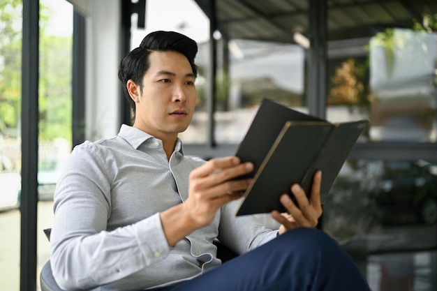 Inteligentny azjatycki biznesmen sprawdzający swój harmonogram spotkań w notatniku
