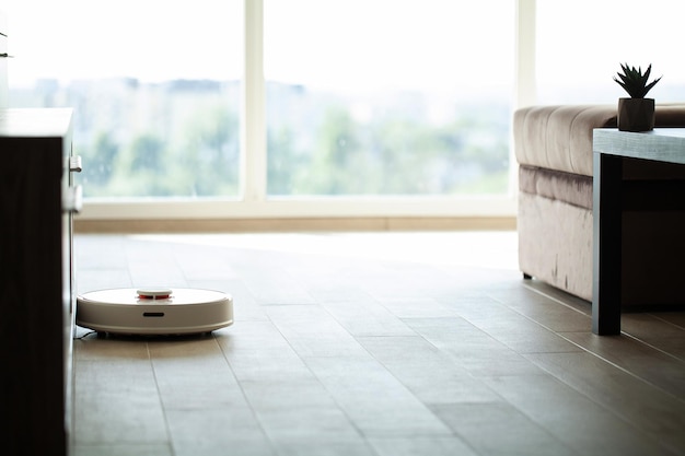 Inteligentny dom. Robot odkurzający porusza się po drewnianej podłodze w salonie.