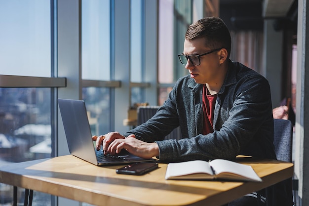 Inteligentny programista siedzący przy biurku w przestrzeni coworkingowej z laptopem i tworzący pomysł na publikację za pomocą netbooka do przesyłania wiadomości i pracy w sieci podczas pracy na zlecenie