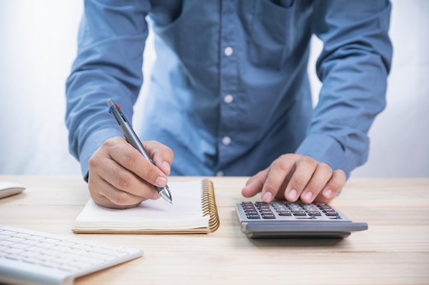 Internet online Koncepcja biznesowa i sieciowa Dorosły biznesmen trzymający długopis do zapisu na kalkulatorze użytku notebooka oblicza zysk biznesowy na drewnianym biurku w biurze z miejscem na kopię