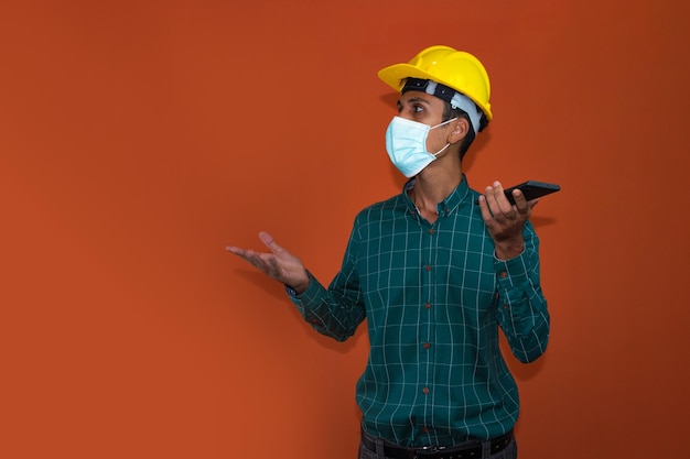 Inżynier architekt lub pracownik z żółtym kaskiem i maską pandemiczną na białym tle Inżynier w pracy rozmawia przez telefon komórkowy