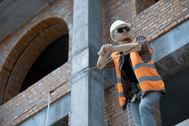 Inżynier budownictwa na wysokości w pomarańczowej kamizelce, białym kasku i okularach przeciwsłonecznych