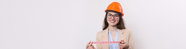 Inżynier dziewczyna w pomarańczowym kasku budowlanym z miarką w dłoniach na białym tle