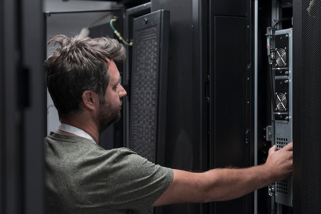 Inżynier IT pracujący w serwerowni lub data center. Technik umieszcza w szafie nowy serwer korporacyjnego superkomputera typu mainframe lub farmę wydobywczą kryptowalut.