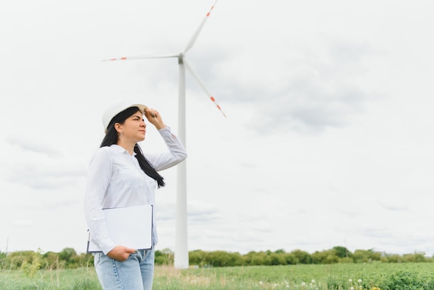 Inżynier kobiet pracuje i trzyma raport na farmie turbin wiatrowych Power Generator Station na górze