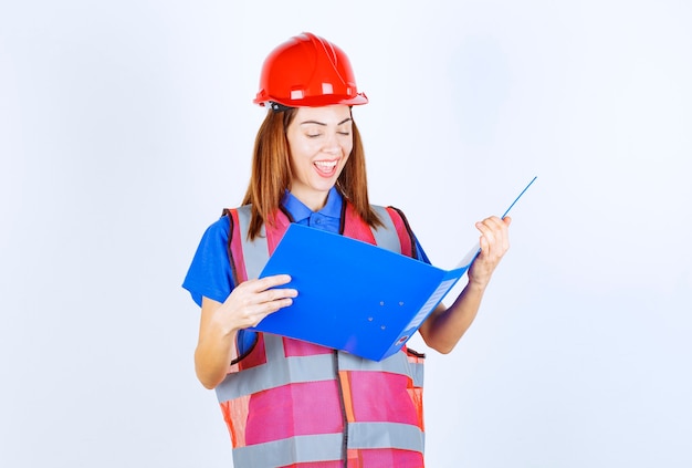 Inżynier kobieta w czerwonym kasku trzyma niebieski folder projektu.