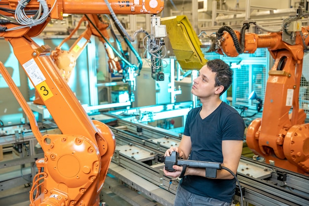 Inżynier kontroluje za pomocą zdalnego sterowania robotem przemysłowym w fabryce. Automatyczne spawanie i klejenie za pomocą automatyzacji i ramion robotów