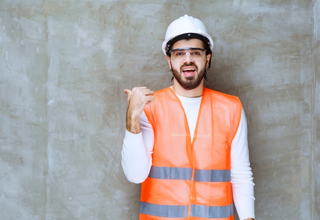 Inżynier mężczyzna w białym kasku i okularach ochronnych, wskazując na kolegę lub coś na boku.