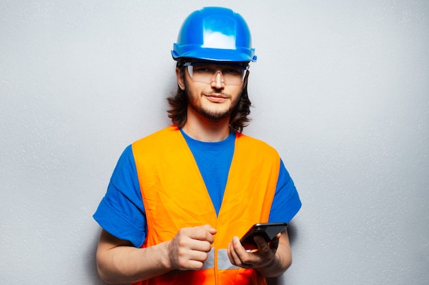 Inżynier młody pracownik budowlany noszący sprzęt bezpieczeństwa trzymający telefon na białym tle