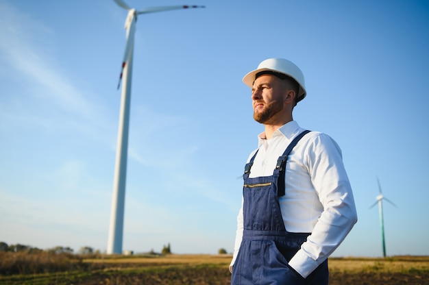 Inżynier sprawdza produkcję energii na turbinie wiatrowej. Pracownik w parku wiatraków w kasku.