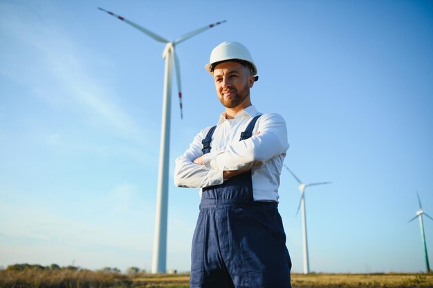 Inżynier sprawdza produkcję energii na turbinie wiatrowej. Pracownik w parku wiatraków w kasku.