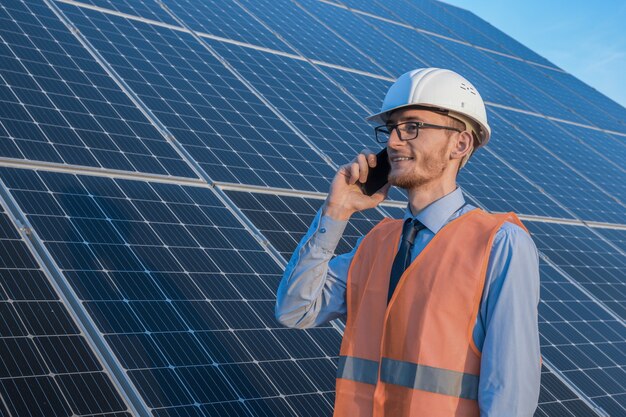 Inżynier w mundurze stojącym na tle paneli słonecznych Farma słoneczna rozmawia przez telefon