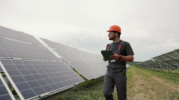 Inżynier z cyfrowym tabletem PC w pobliżu nowoczesnych fotowoltaicznych paneli słonecznych. Produkcja czystej energii. Farma słoneczna.