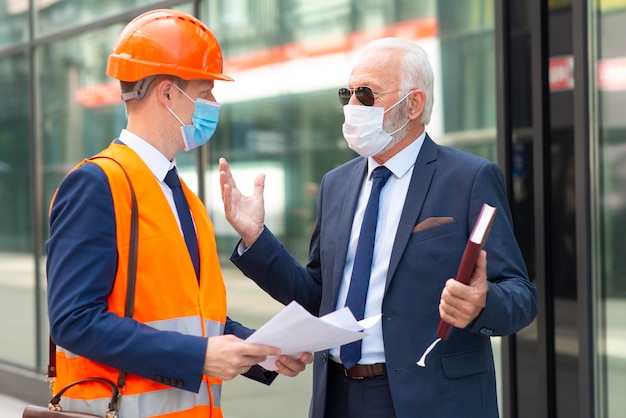 Zdjęcie inżynier z maską rozmawiający o czymś ze starszym biznesmenem w masce