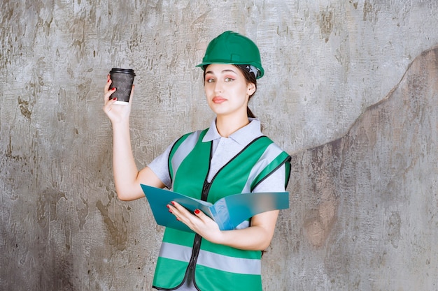 Inżynierka W Zielonym Mundurze I Hełmie, Trzymająca Czarną Filiżankę Kawy I Niebieski Folder Projektu