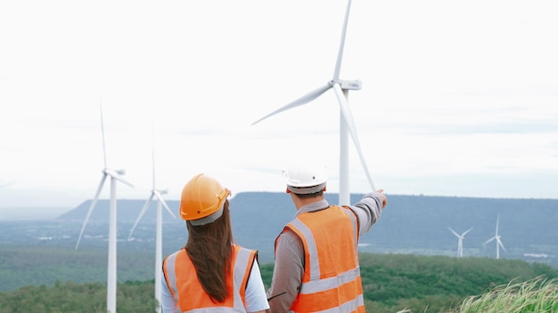 Inżynierowie i inżynierki pracujący na farmie wiatrowej na szczycie wzgórza lub góry na wsi Progresywny ideał dla przyszłej produkcji odnawialnej, zrównoważonej energii