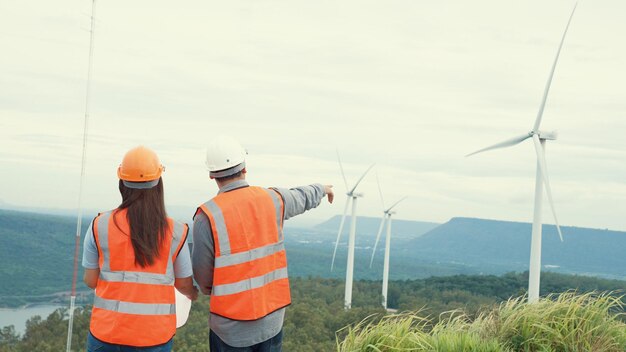 Inżynierowie płci męskiej i żeńskiej pracujący na farmie wiatrowej na szczycie wzgórza lub góry na obszarach wiejskich Postępowy ideał dla przyszłej produkcji odnawialnej, zrównoważonej energii