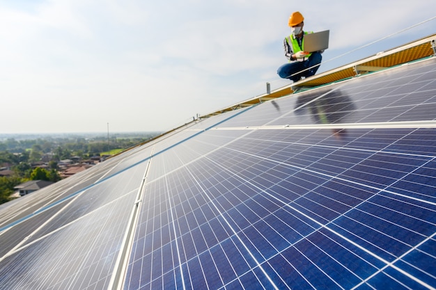 Inżynierowie używają laptopa do badania paneli słonecznych na dachu domu, w którym panele słoneczne są zainstalowane przy użyciu energii słonecznej.
