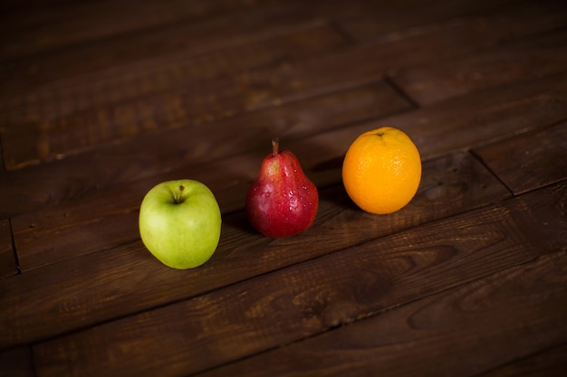 Jabłko, gruszka i pomarańcza na drewnianym stole