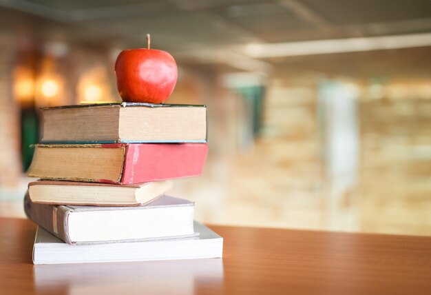 Zdjęcie jabłko na książkach na stole z półką na tle biblioteki koncepcja edukacji i uczenia się z stosem książek