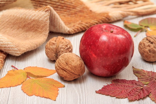 Jabłko, orzechy włoskie, kratkę w kratkę i suche liście na drewnianych deskach. Jesienny motyw.