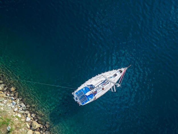 Jachty żaglowe bez żagli na kotwicy i linii zacumowania na morzu, widok lotniczy z drona