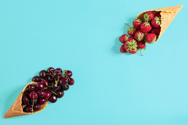 Jagody w rożkach waflowych truskawka i czarna wiśnia na niebieskim ba