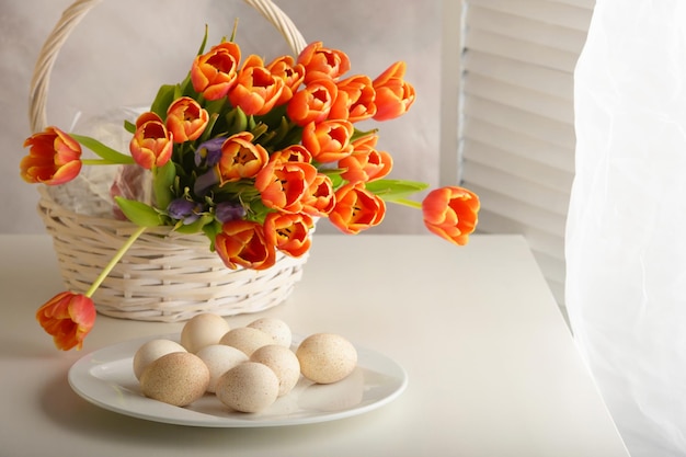 Jaja indycze w białych naczyniach i bukiet pomarańczowych tulipanów na jasno barwionej drewnianej powierzchni Poziomo