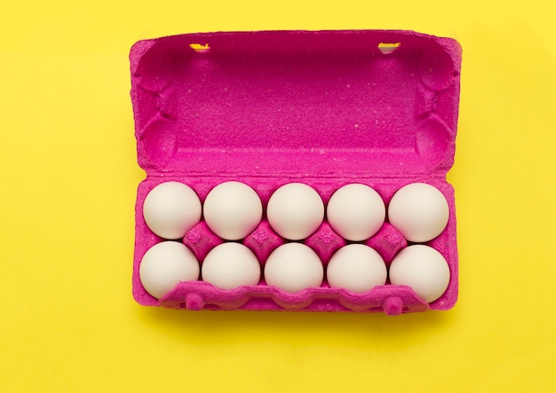 Jaja kurze w różowym pudełku na jajka na żółtym tle. kupowanie jajek przed Wielkanocą.