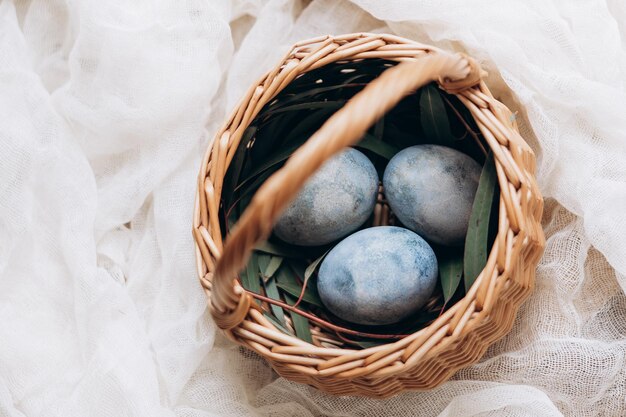 Jaja wielkanocne w pastelowych kolorach w małym wiklinowym koszu na jasnym tle Minimalna koncepcja świętowania Wielkanocy barwione jaja kurze