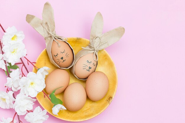 Jajka estrowe pomalowane jak króliczek w drewnianym kubku na różowym biurku