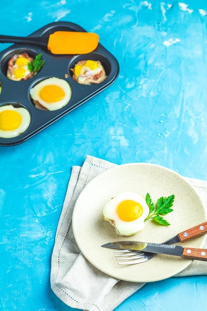 Jajka pieczone w lekkim talerzu i foremkach do pieczenia Porcjowana zapiekanka z bekonu i jajek w stylu włoskim Niebieskie betonowe tło powierzchni stołu