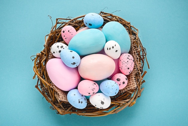 Jajka pomalowane na niebiesko i różowo na niebieskim tle w koszyku gniazdowym na niebieskim tle