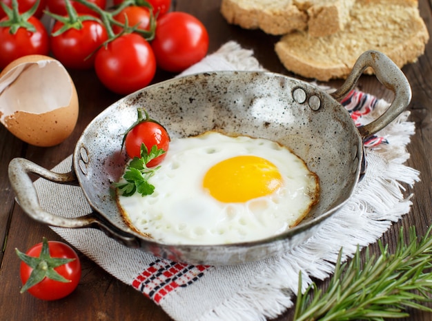 Jajka sadzone z pomidorami, domowym chlebem i ziołami na starej patelni na drewnie