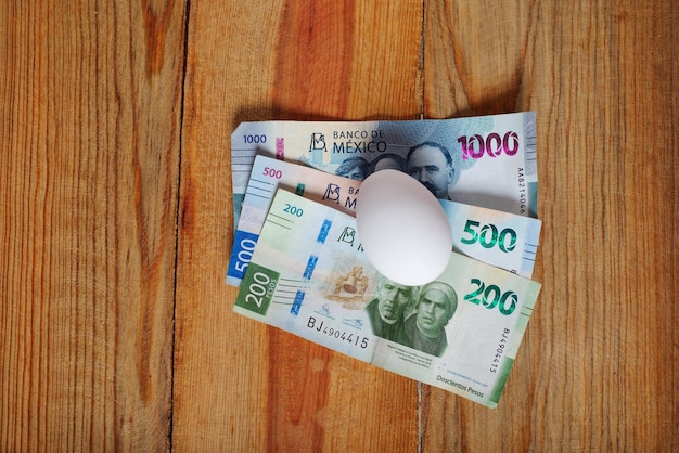 Jajko i meksykańskie banknoty na drewnianym stole Koncepcja rosnących kosztów produkcji i konsumpcji jaj