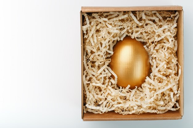 Jajko robić złoto w drewnianym pudełku na białym tle. Pojęcie wyłączności i superprize. Minimalistyczna kompozycja.