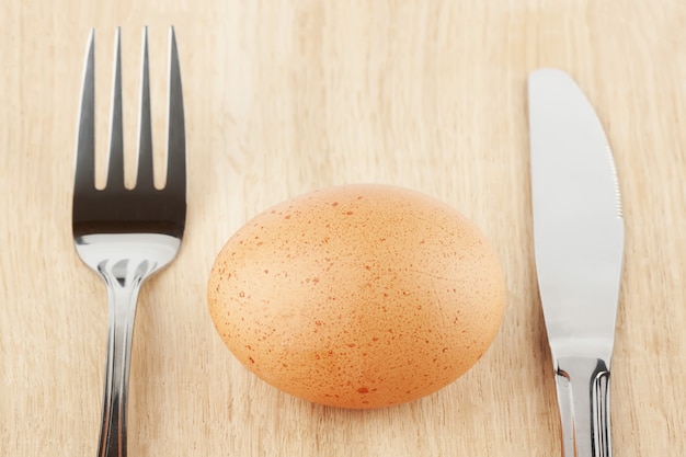 Jajko z widelcem i nożem na drewnianym stole