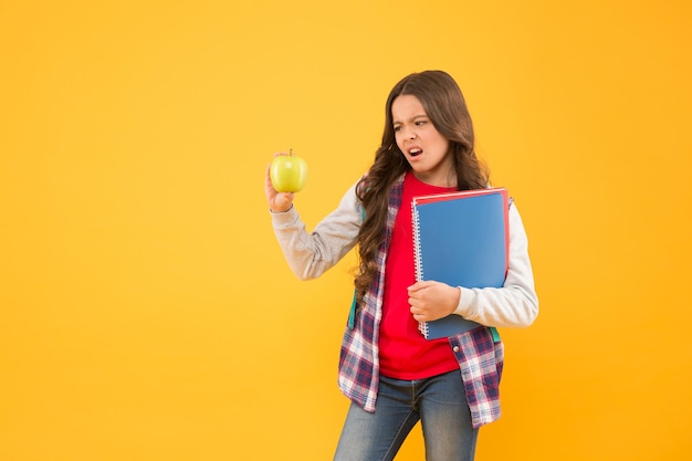 Jak nauczyć się lubić jeść jabłko Nieszczęśliwe dziecko trzyma jabłko żółte tło Przerwa w szkole Edukacja zdrowotna Ekologiczna przekąska Kształtowanie zdrowych nawyków żywieniowych Naturalna dieta