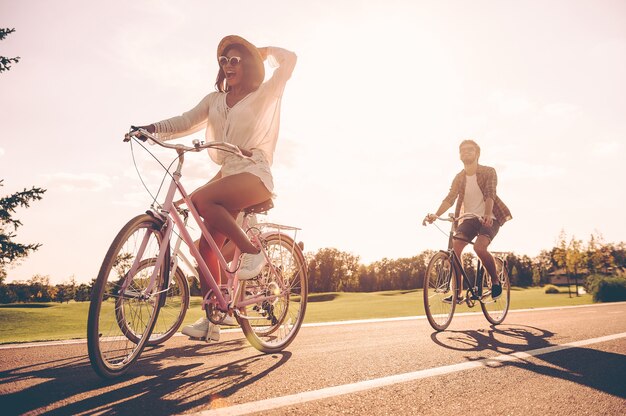 Jaki wspaniały dzień! Niski kąt widzenia młodych ludzi jeżdżących rowerami wzdłuż drogi i wyglądających na szczęśliwych