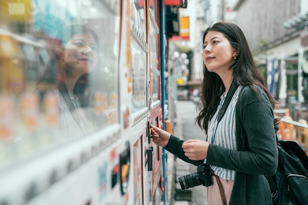 Japonia automat. Młoda kobieta turysta wybierając przekąskę lub napój w automacie. pani wrzucająca monety do automatu sprzedającego na japońskiej ulicy.