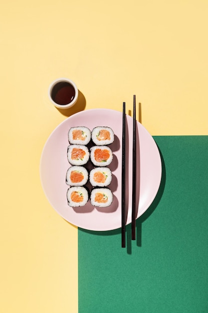 Japońska rolka sushi z ogórkiem łososiowym i sosem sojowym z pałeczkami w różowym talerzu na żółtym i zielonym tle z twardym cieniem Widok z góry i miejsce na kopię