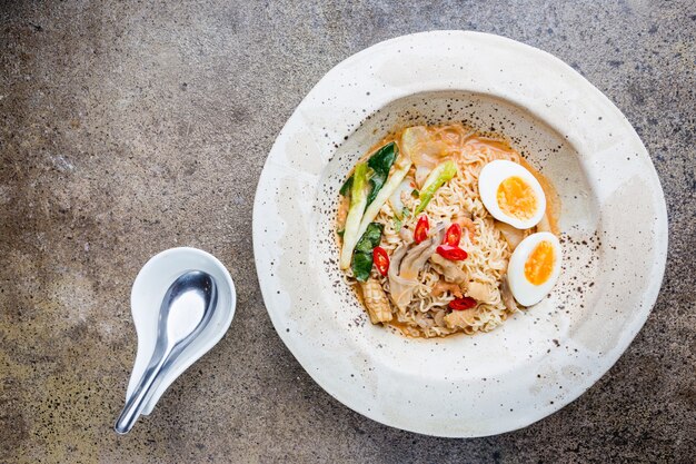 Japoński makaron ramen z kurczakiem, grzybami shiitake i jajkiem w białej misce, widok z góry