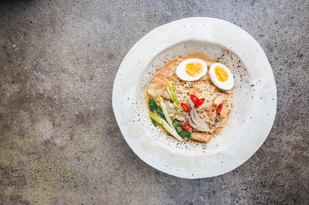 Japoński makaron ramen z kurczakiem, grzybami shiitake i jajkiem w białej misce, widok z góry