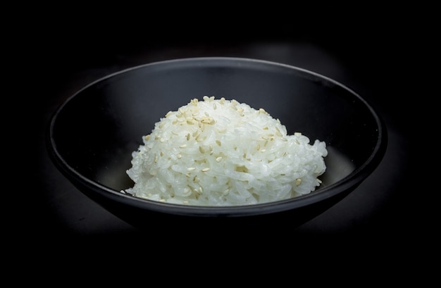 Japoński ryż posypany białym sezamem na czarnej misce.